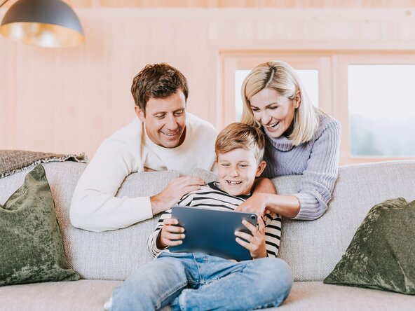 Familie sitzt in Wohnzimmer auf Sofa und spielt mit Tablet